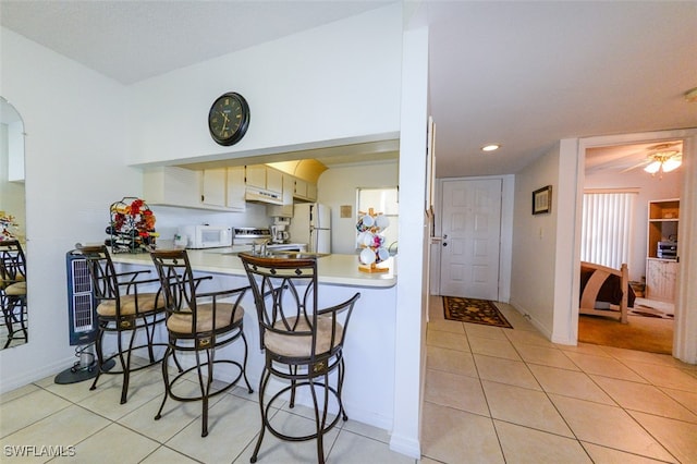 kitchen featuring ceiling fan, kitchen peninsula, white appliances, a breakfast bar area, and light tile patterned flooring