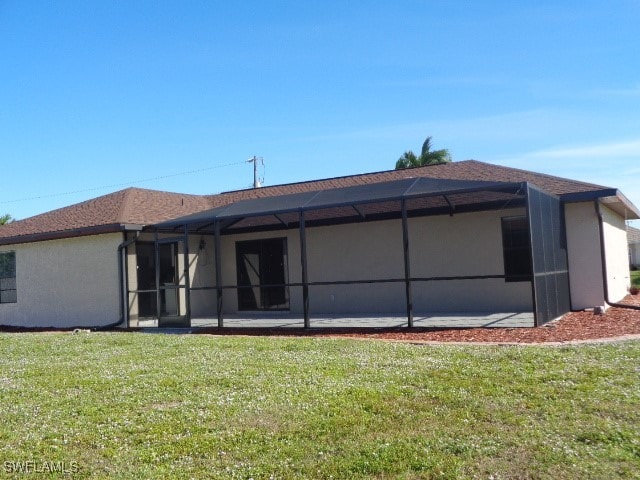 rear view of house featuring a lawn and glass enclosure