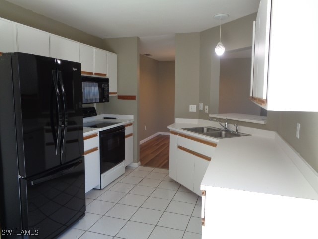 kitchen with sink, kitchen peninsula, decorative light fixtures, white cabinets, and black appliances