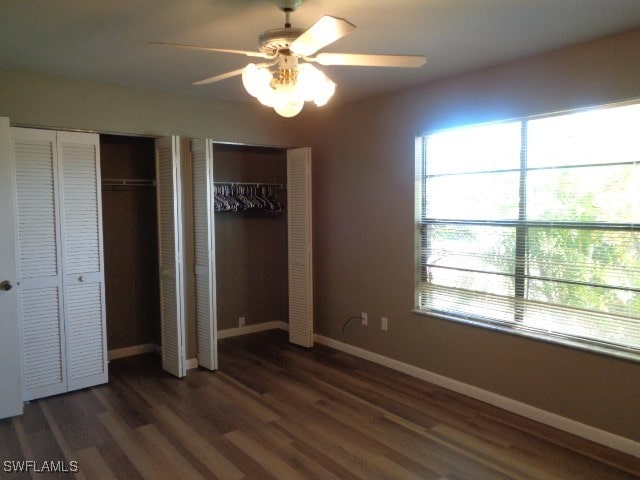 unfurnished bedroom with ceiling fan, dark wood-type flooring, and two closets