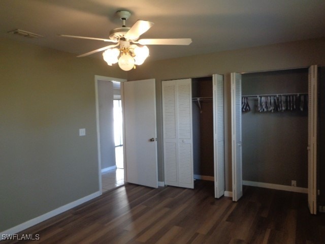 unfurnished bedroom with multiple closets, ceiling fan, and dark wood-type flooring