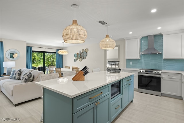 kitchen featuring appliances with stainless steel finishes, white cabinetry, hanging light fixtures, and wall chimney range hood