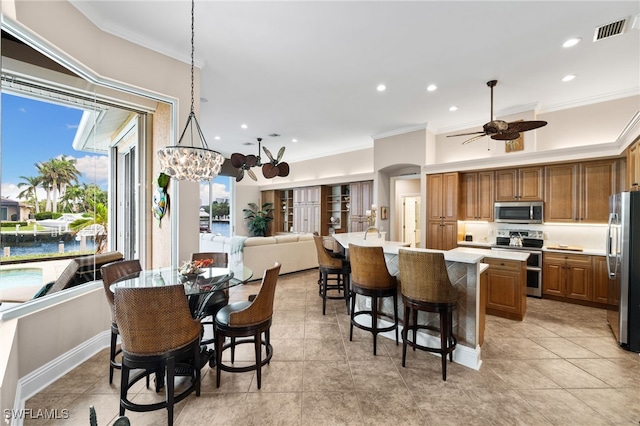 kitchen with pendant lighting, ornamental molding, stainless steel appliances, and an island with sink