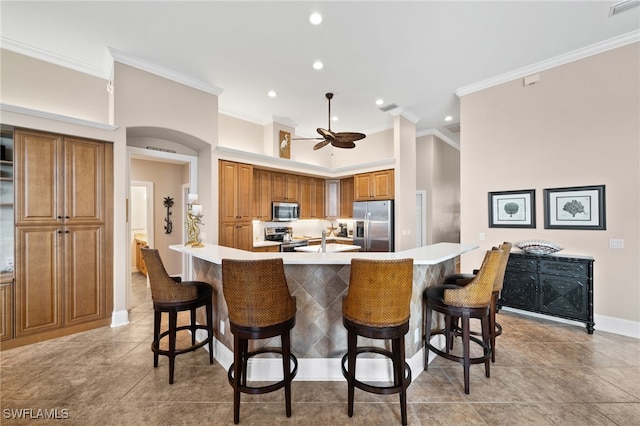 kitchen with appliances with stainless steel finishes, ceiling fan, crown molding, and a breakfast bar area