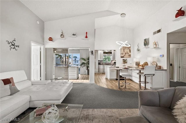 living room featuring high vaulted ceiling, light hardwood / wood-style flooring, and a notable chandelier