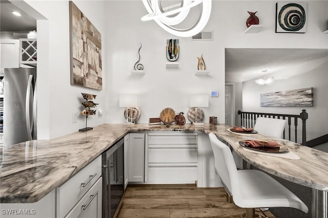 kitchen with a kitchen bar, white cabinetry, stainless steel fridge, kitchen peninsula, and beverage cooler