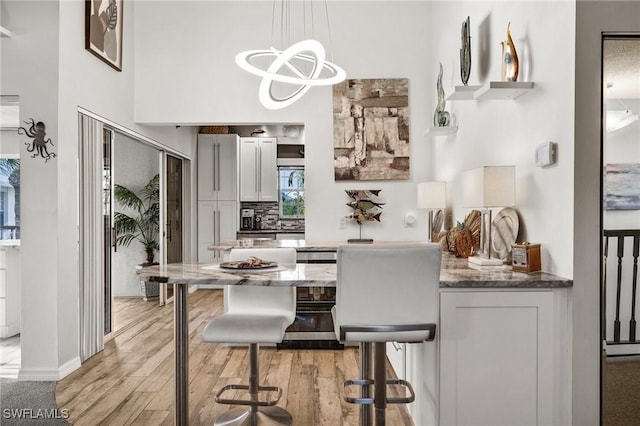 interior space featuring pendant lighting, stone counters, a kitchen breakfast bar, white cabinets, and light wood-type flooring