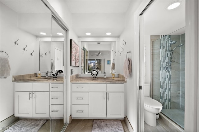 bathroom with toilet, wood-type flooring, vanity, a shower with door, and ceiling fan