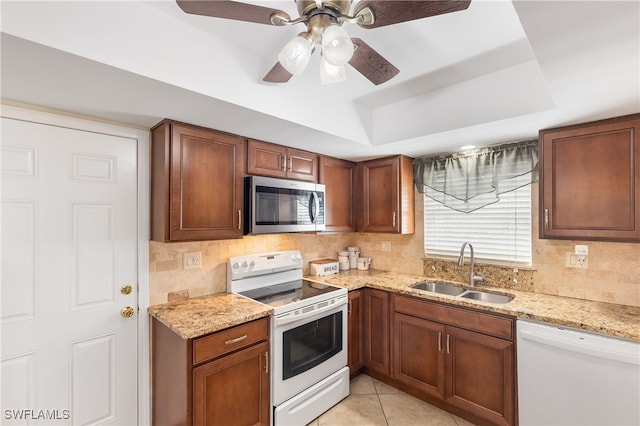 kitchen with light stone countertops, white appliances, a raised ceiling, sink, and light tile patterned floors