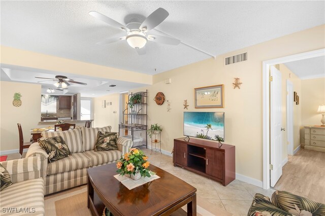 living room featuring ceiling fan, light hardwood / wood-style floors, and a textured ceiling