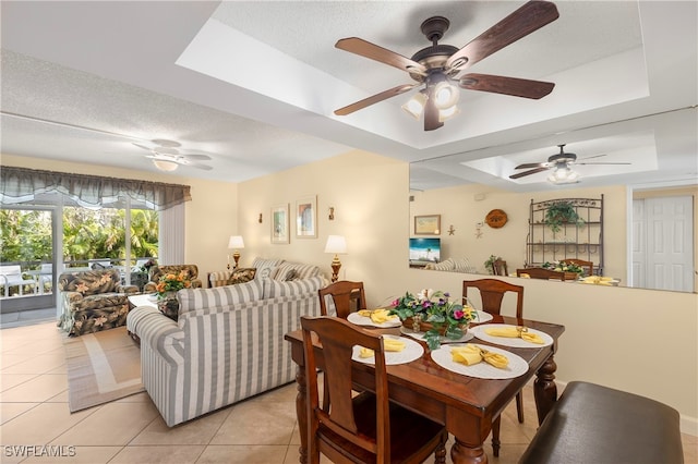 dining room with ceiling fan, light tile patterned flooring, a textured ceiling, and a tray ceiling