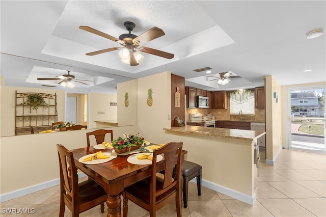 dining room featuring ceiling fan, sink, a textured ceiling, a tray ceiling, and light tile patterned flooring