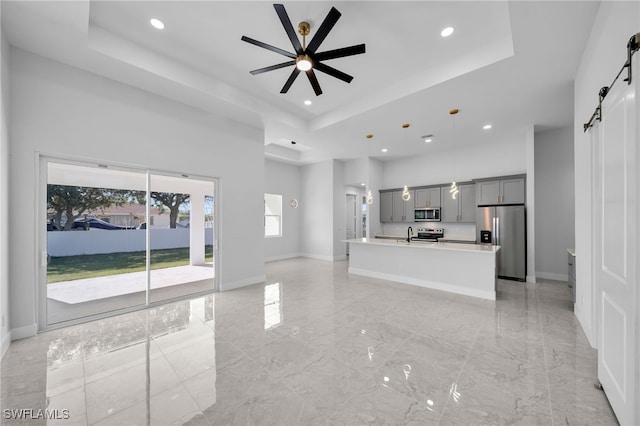 unfurnished living room featuring a raised ceiling, a barn door, ceiling fan, and a towering ceiling