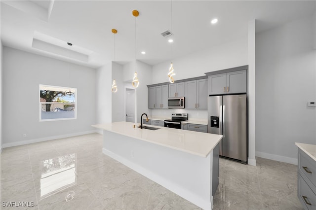 kitchen featuring pendant lighting, stainless steel appliances, gray cabinetry, and an island with sink