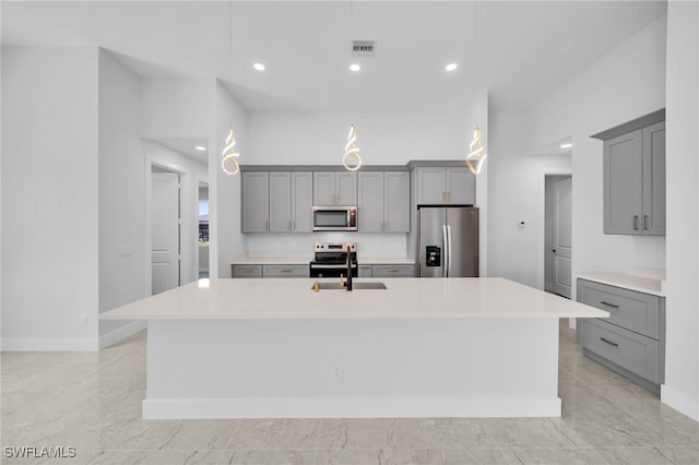 kitchen featuring hanging light fixtures, stainless steel appliances, a kitchen island with sink, and gray cabinetry