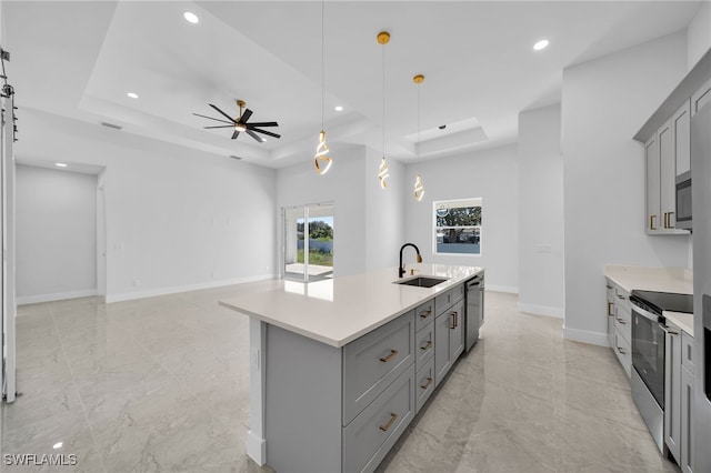 kitchen featuring a tray ceiling, a kitchen island with sink, sink, and appliances with stainless steel finishes