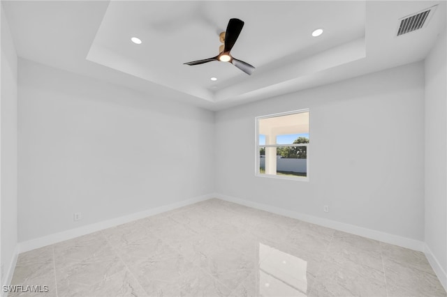 empty room with ceiling fan and a raised ceiling