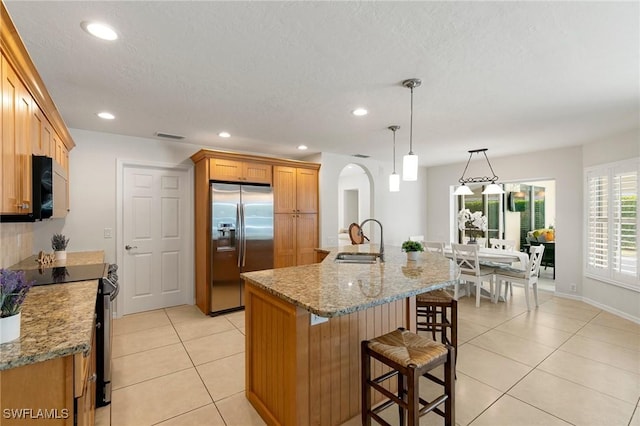 kitchen featuring a center island with sink, sink, pendant lighting, electric range oven, and stainless steel fridge