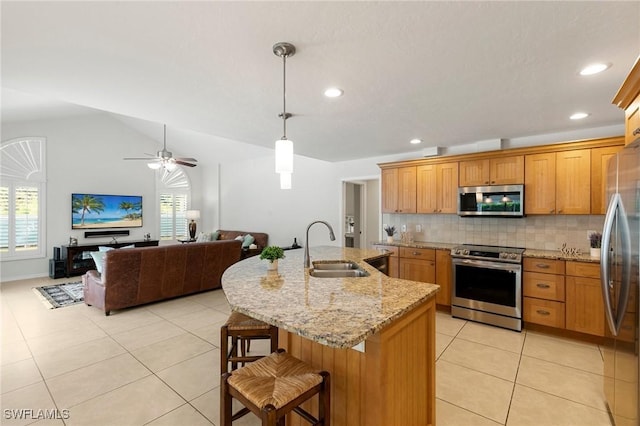 kitchen featuring appliances with stainless steel finishes, sink, light tile patterned floors, decorative light fixtures, and a kitchen island with sink