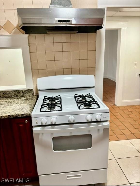 kitchen featuring decorative backsplash, light stone countertops, exhaust hood, light tile patterned floors, and white range with gas stovetop