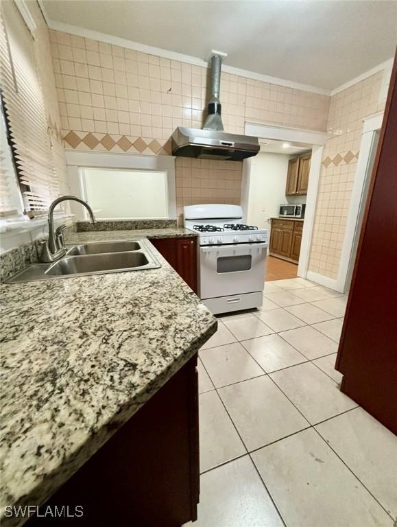 kitchen with wall chimney range hood, gas range gas stove, sink, and tile walls