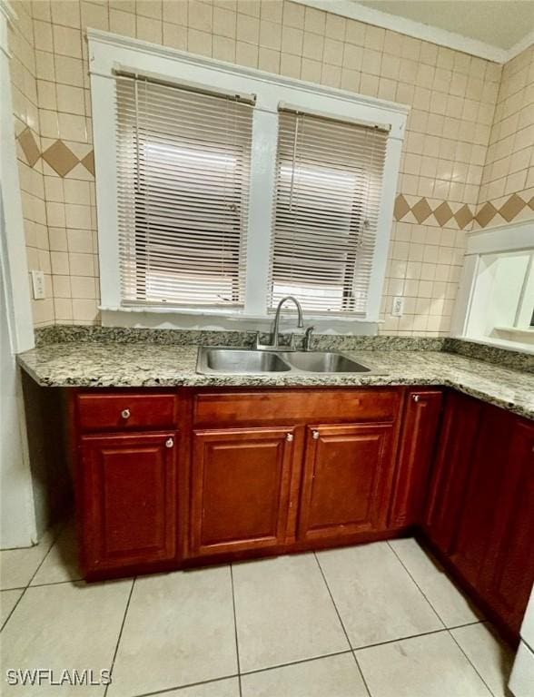 kitchen featuring light tile patterned flooring, light stone counters, sink, and tile walls