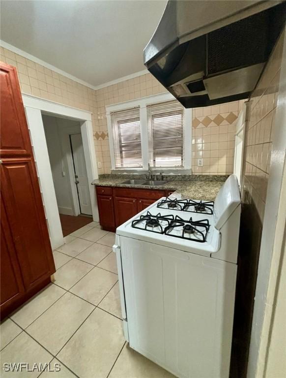 kitchen featuring sink, white gas range oven, light tile patterned floors, exhaust hood, and ornamental molding