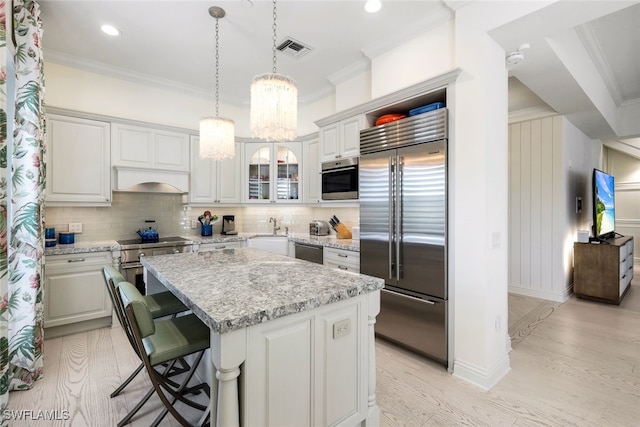 kitchen featuring light stone countertops, light wood-type flooring, stainless steel appliances, white cabinets, and a kitchen island