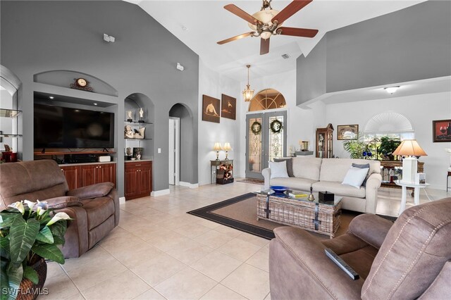 living room featuring built in features, high vaulted ceiling, light tile patterned flooring, ceiling fan with notable chandelier, and french doors