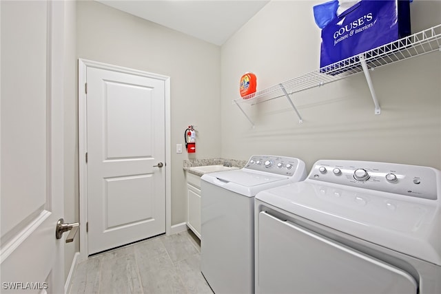 clothes washing area with washer and clothes dryer, light hardwood / wood-style flooring, cabinets, and sink