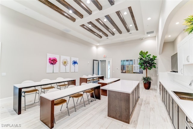 kitchen with beam ceiling, sink, a kitchen island, light hardwood / wood-style floors, and white cabinets