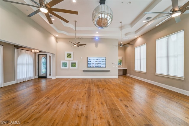 unfurnished living room with a chandelier, a high ceiling, light wood-type flooring, and a raised ceiling