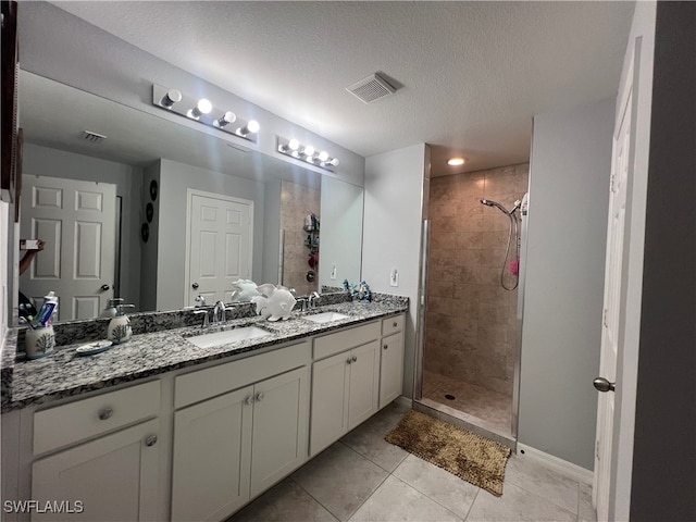 bathroom with tile patterned flooring, tiled shower, a textured ceiling, and vanity