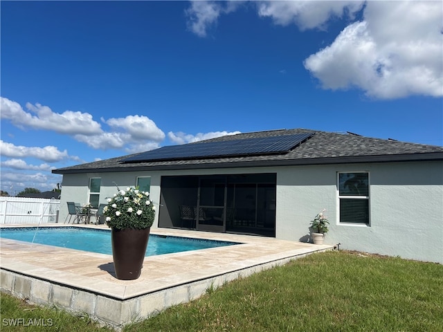 rear view of house featuring solar panels and a fenced in pool