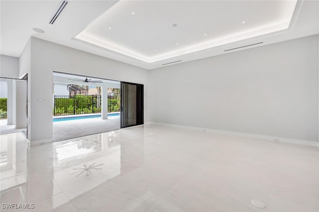 empty room featuring ceiling fan, light tile patterned floors, and a tray ceiling