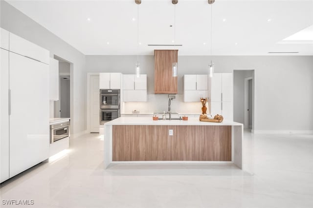 kitchen with double oven, sink, decorative light fixtures, white cabinets, and an island with sink