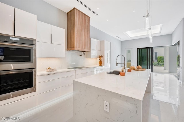 kitchen featuring pendant lighting, white cabinetry, a kitchen island with sink, and double oven