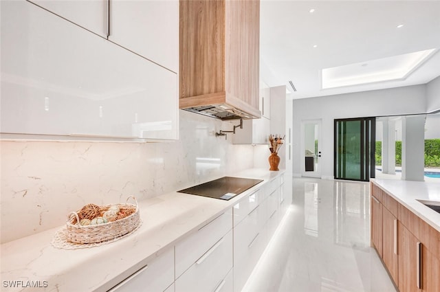 kitchen featuring white cabinets, wall chimney range hood, a skylight, decorative backsplash, and black electric cooktop