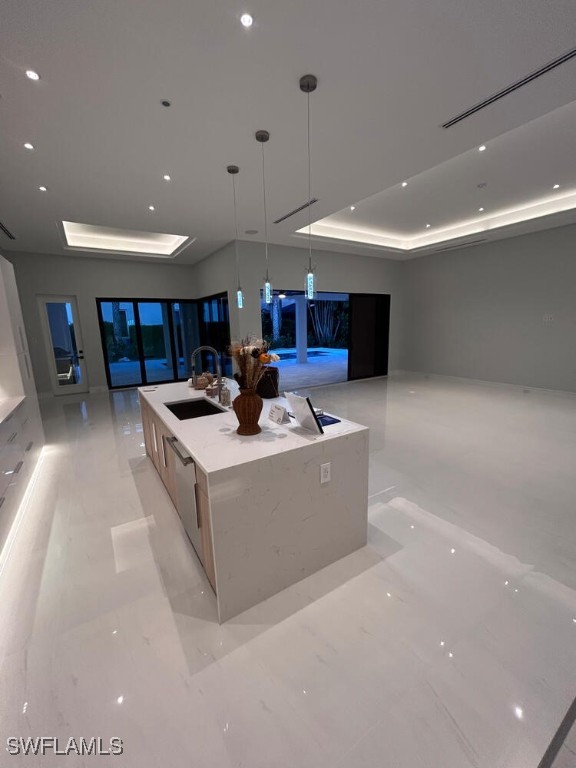 interior space with a large island, sink, light stone counters, pendant lighting, and a tray ceiling