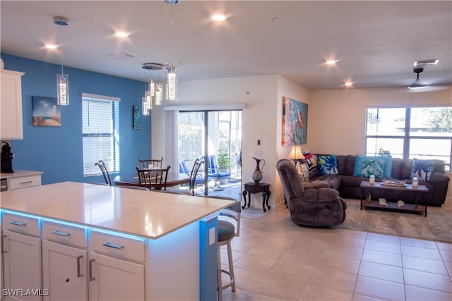 kitchen featuring a breakfast bar, white cabinets, light tile patterned floors, decorative light fixtures, and a kitchen island