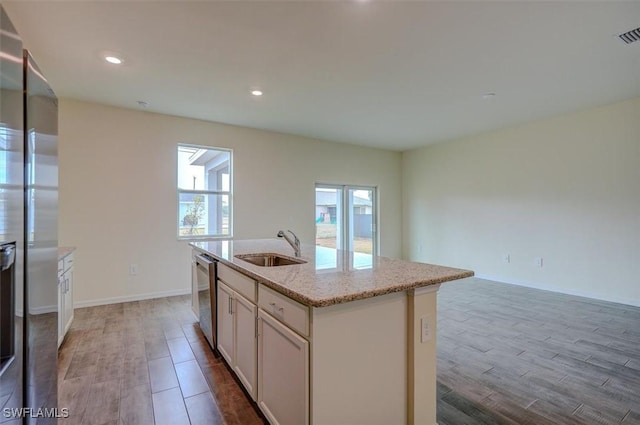 kitchen featuring a center island with sink, light stone counters, stainless steel appliances, and sink