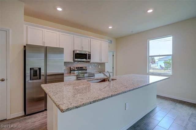 kitchen with sink, stainless steel appliances, white cabinetry, and an island with sink