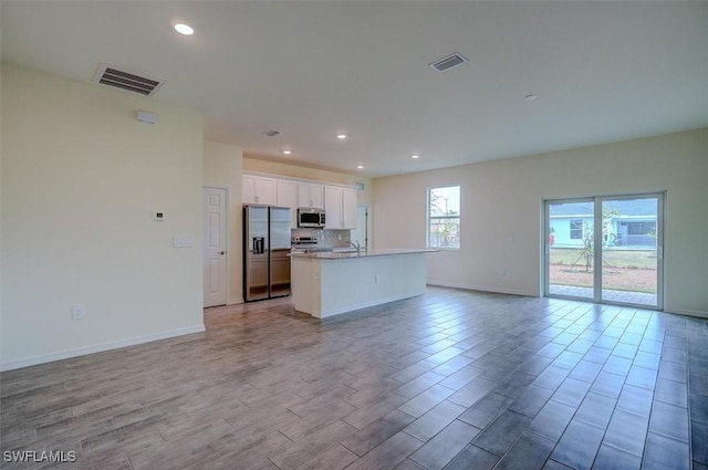 kitchen with white cabinets, stainless steel appliances, tasteful backsplash, and a center island with sink