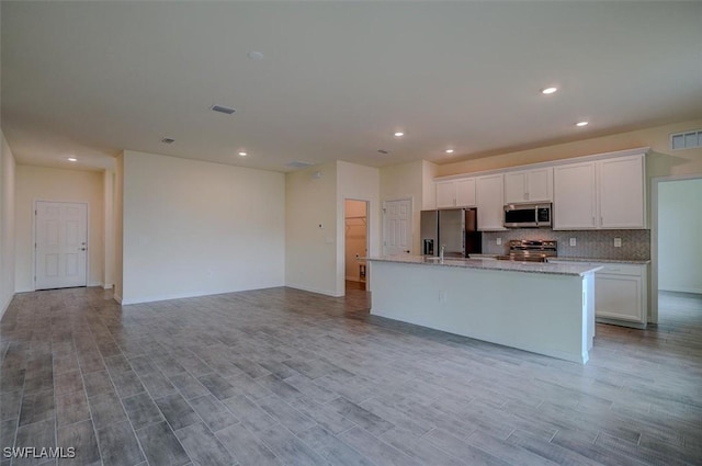 kitchen with stainless steel appliances, light stone counters, backsplash, a center island with sink, and white cabinets