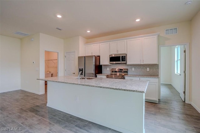 kitchen featuring a kitchen island with sink, white cabinets, sink, appliances with stainless steel finishes, and light stone counters