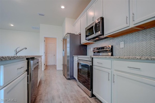 kitchen featuring backsplash, light stone counters, stainless steel appliances, light hardwood / wood-style floors, and white cabinetry