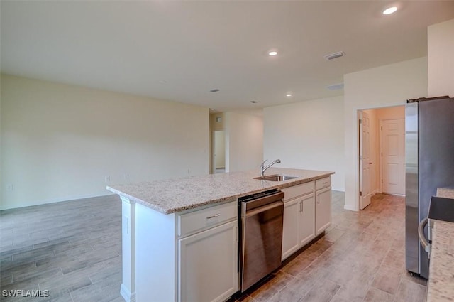 kitchen featuring light stone countertops, white cabinetry, sink, a center island with sink, and appliances with stainless steel finishes