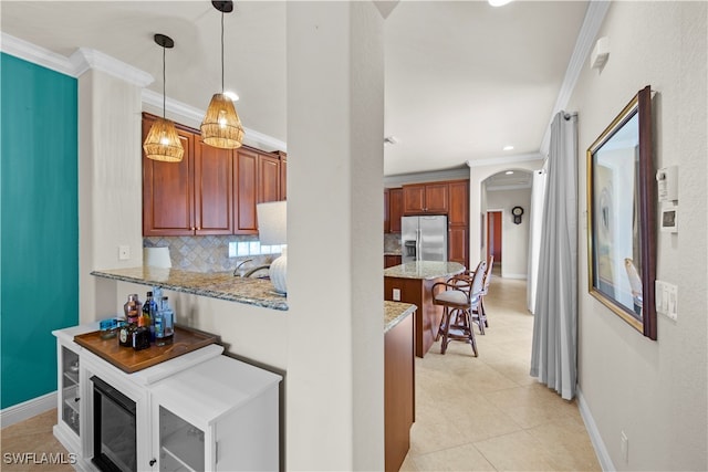 kitchen featuring stainless steel fridge, hanging light fixtures, light stone counters, ornamental molding, and decorative backsplash