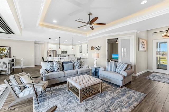 living room featuring crown molding, a raised ceiling, dark wood-type flooring, and ceiling fan with notable chandelier