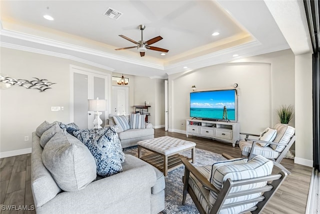 living room featuring hardwood / wood-style flooring, ceiling fan with notable chandelier, crown molding, and a tray ceiling